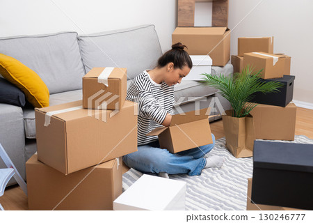 Fresh Start: A woman, new homeowner or renter, sits among boxes, opening packages in her brand-new space, symbolizing new beginnings 130246777