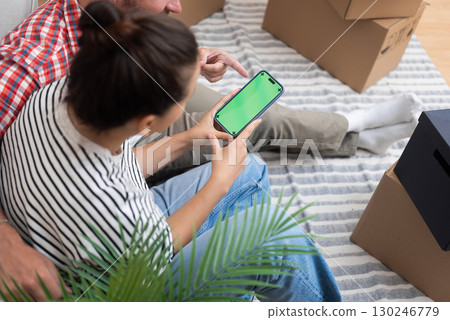A young couple holds a smartphone with a chroma key screen mock-up, online shopping for new home decor and furniture 130246779