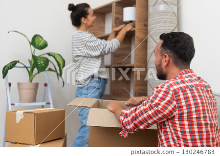 happy young family moves into their new home, husband and wife unpacking and adorning an empty shelf with a lamp, capturing the essence of relocation 130246783