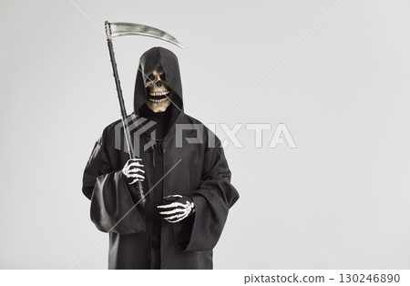 Man in grim reaper death costume isolated on studio gray background holding scythe 130246890