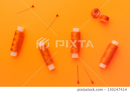 Orange sewing threads and pins on bright background 130247414