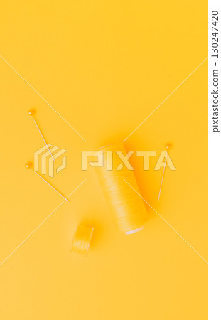 Yellow sewing thread and pins on bright background Yellow sewing thread and pins on bright background 130247420