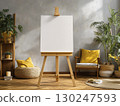 Cozy and stylish interior space with empty canvas wooden easel, surrounded by plants, woven pouf with yellow pillow, wooden chair with yellow cushion, and decorative items creating warm atmosphere 130247593