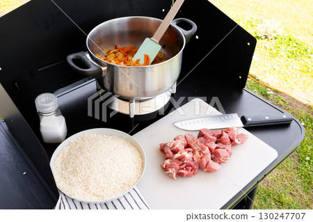 Outdoor cooking setup with pot and ingredients for rice and meat dish 130247707