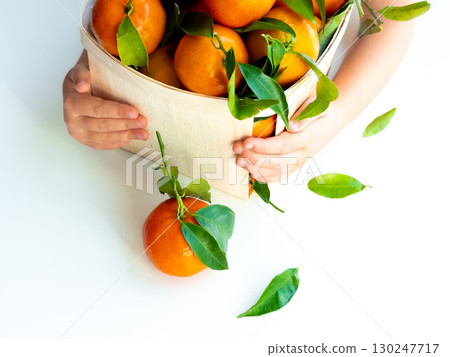 Child holding a basket of fresh oranges with green leaves Child holding a basket of fresh oranges with green leaves 130247717