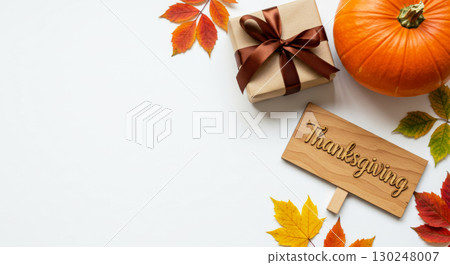 Thanksgiving background with a pumpkin, gift, wooden sign, and autumn leaves on a white surface with copy space. 130248007