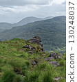 A serene landscape unfolds, revealing the lush green hills and rugged rock formations within the Gap of Dunloe. Cloudy skies provide a soft light over the mountainous terrain in Ireland. 130248037