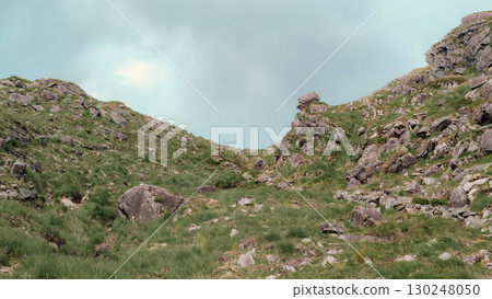 This captures a view looking up through the Gap of Dunloe. The rocky terrain is covered with green grass, creating a rugged landscape. It is located in County Kerry, Ireland. This captures a view looking up through the Gap of Dunloe. The rocky terrain is covered with green grass, creating a rugged landscape. It is located in County Kerry, Ireland. 130248050