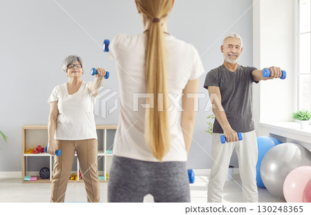 Elderly mature people group exercising with dumbbells with fitness trainer in gym. 130248365