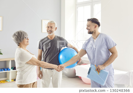 Active cheerful attractive fit senior woman, man coach hand shake holding fitness ball, working out 130248366