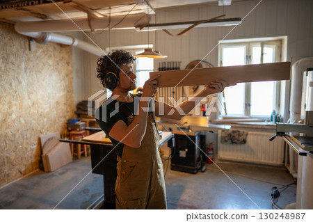 Craftsman checking wooden plank carefully before crafting in carpentry studio, focused manual work Craftsman checking wooden plank carefully before crafting in carpentry studio, focused manual work 130248987