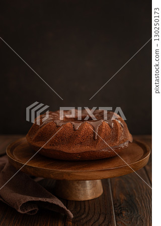 Chocolate cake with chocolate icing on dark wooden table. Low key. Front view Chocolate cake with chocolate icing on dark wooden table. Low key. Front view 130250173