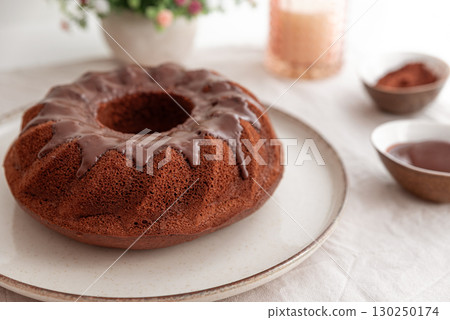 Chocolate cake with chocolate icing on white wooden table. 130250174