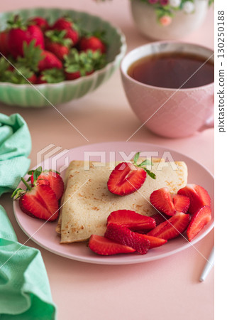 Crepes with chocolate spread and fresh strawberries, served with tea on pink background Crepes with chocolate spread and fresh strawberries, served with tea on pink background 130250188