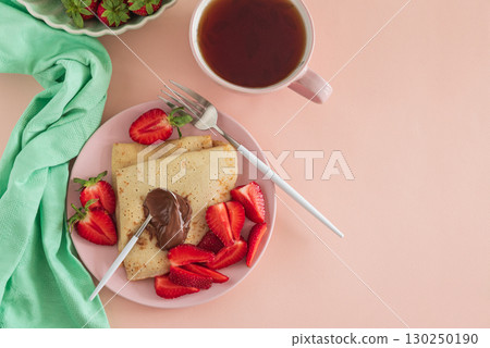 Crepes with chocolate spread and fresh strawberries, served with tea on pink background. Top view Crepes with chocolate spread and fresh strawberries, served with tea on pink background. Top view 130250190