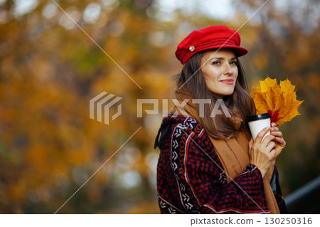 pensive modern woman in red hat with autumn leafs 130250316