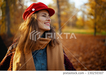 smiling modern female in red hat with scarf in city park 130250387
