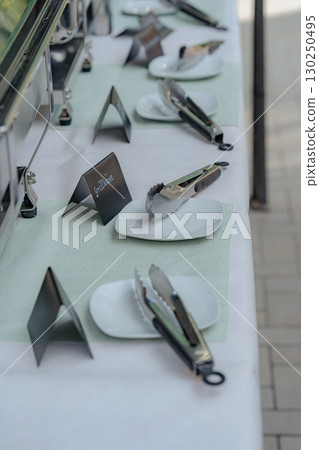 Close-up view of a buffet table prepared for guests, featuring white square plates, serving tongs, and black food labels. Elegant catering setup for events, weddings, or parties. Ideal for Close-up view of a buffet table prepared for guests, featuring white square plates, serving tongs, and black food labels. Elegant catering setup for events, weddings, or parties. Ideal for 130250495