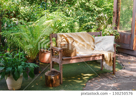 Wooden garden bench with yellow blanket and straw basket, place fo relax in cozy summer backyard Wooden garden bench with yellow blanket and straw basket, place fo relax in cozy summer backyard 130250576