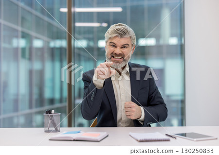 Businessman in formal attire expressing anger and frustration while pointing in an office setting. 130250833