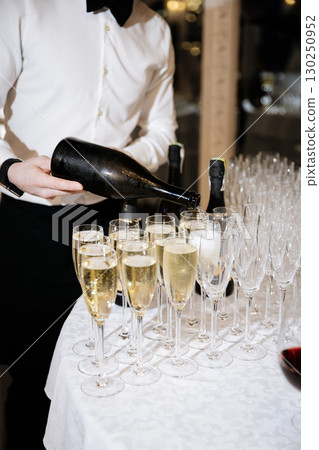 Waiter pouring champagne into flutes at elegant evening reception event 130250952