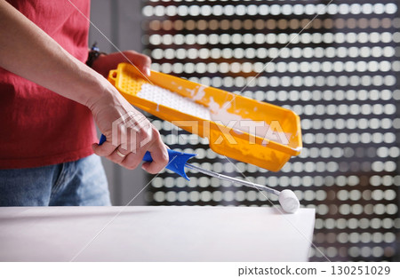 Girl Uses A Roller To Paint A Wooden Board White On The Surface Of A Big White Table Girl Uses A Roller To Paint A Wooden Board White On The Surface Of A Big White Table 130251029