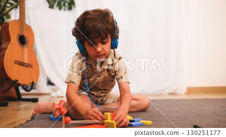 Young child playing with building blocks while listening to music on headphones 130251177
