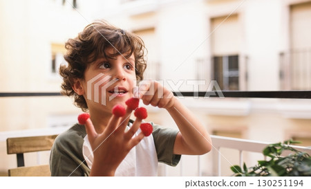 Smiling child playing with raspberries on balcony: healthy eating habits Smiling child playing with raspberries on balcony: healthy eating habits 130251194