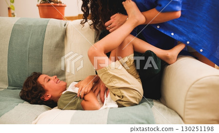 Mother and son tickling and laughing on sofa at home 130251198