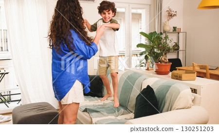 Happy mother and son dancing and jumping on sofa at home Happy mother and son dancing and jumping on sofa at home 130251203