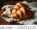 Freshly baked croissants placed on a rustic wooden table, resting on a soft, white linen cloth.  130251215