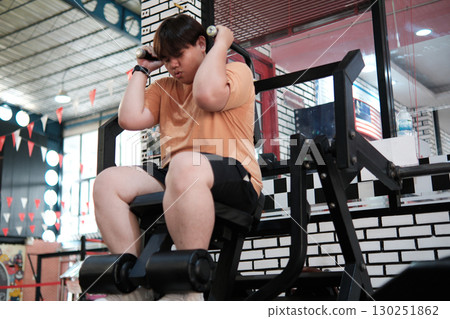 A determined plus-size man shows great effort and struggle on an abdominal crunch machine during a gym workout. 130251862