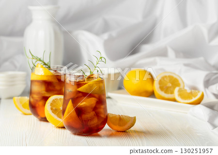 Iced tea or alcoholic cocktail with ice, rosemary and lemon slices on the white table. Iced tea or alcoholic cocktail with ice, rosemary and lemon slices on the white table. 130251957