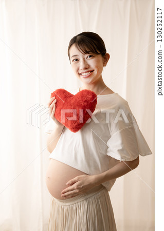 Eight-month pregnant woman holding a red heart Eight-month pregnant woman holding a red heart 130252117
