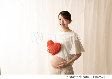 Eight-month pregnant woman holding a red heart 130252122