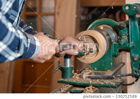 Carpentry. Turnery of a wooden bowl with spiral sawdust shavings with hand and chisel Carpentry. Turnery of a wooden bowl with spiral sawdust shavings with hand and chisel 130252589