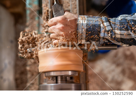 Carpentry. Turnery of a wooden bowl with spiral sawdust shavings with hand and chisel Carpentry. Turnery of a wooden bowl with spiral sawdust shavings with hand and chisel 130252590