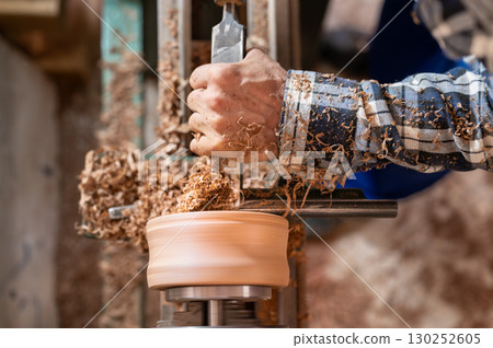 Carpentry. Turnery of a wooden bowl with spiral sawdust shavings with hand and chisel Carpentry. Turnery of a wooden bowl with spiral sawdust shavings with hand and chisel 130252605