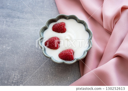 Natural fresh yogurt with raspberry berries in green porcelain plate on the wood table and pink silk napkin for healthy breakfast.  130252613