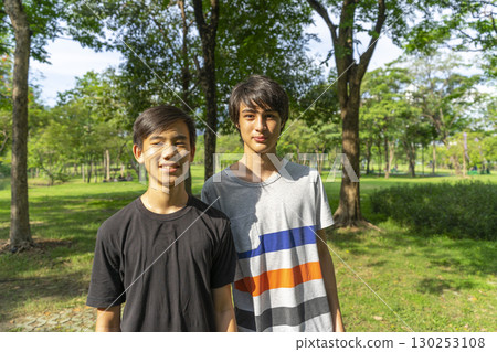 Two joyful teenage boys looking at the camera in the summer park against the blue sky. 130253108