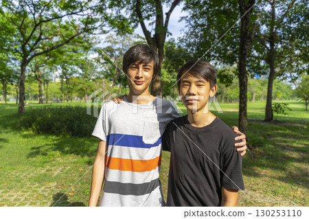 Two joyful teenage boys looking at the camera in the summer park against the blue sky. Two joyful teenage boys looking at the camera in the summer park against the blue sky. 130253110