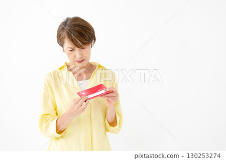 A middle-aged woman looking at her bankbook and worrying 130253274