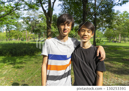 Two joyful teenage boys looking at the camera in the summer park against the blue sky. Two joyful teenage boys looking at the camera in the summer park against the blue sky. 130253391