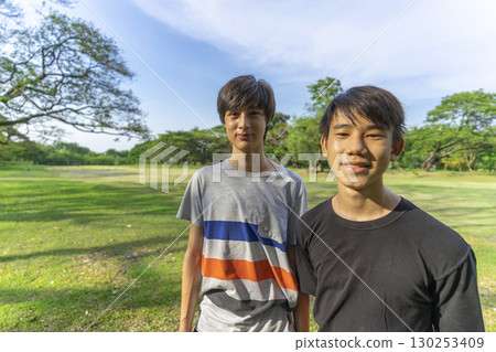 Two joyful teenage boys looking at the camera in the summer park against the blue sky. 130253409