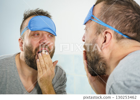 Sleepy man looking at mirror and yawning 130253462