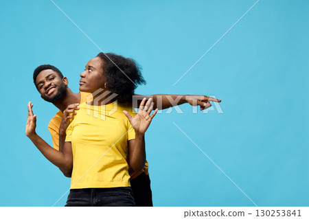 Happy diverse couple posing against a blue background, showcasing playful interaction and vibrant yellow outfits, perfect for joy and diversity themes 130253841