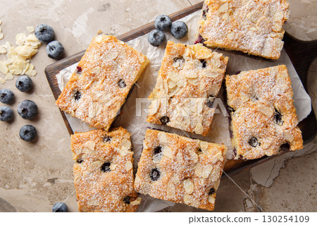 Blueberry Breakfast Cake is bursting with fresh berries and topped with crunchy slivered almonds closeup on the wooden board. Horizontal top view 130254109