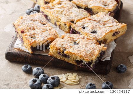 Blueberry Breakfast Cake is bursting with fresh berries and topped with crunchy slivered almonds closeup on the wooden board. Horizontal 130254117