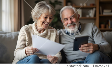 Happy senior couple enjoying time together at home, using smartphone and reading papers 130254741