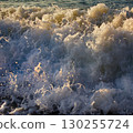Sea rolling and receding water in rays of setting sun. 130255724